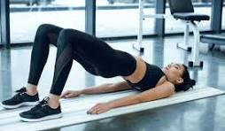 Femme en tenue de sport réalisant un exercice du pont sur un tapis dans une salle de sport