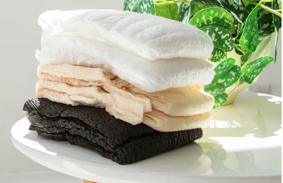 Pile de culottes absorbantes blanches, beiges et noires posées sur une table avec une plante verte